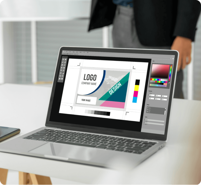 A laptop displaying a graphic design software interface with a logo design project open, set on a white desk.